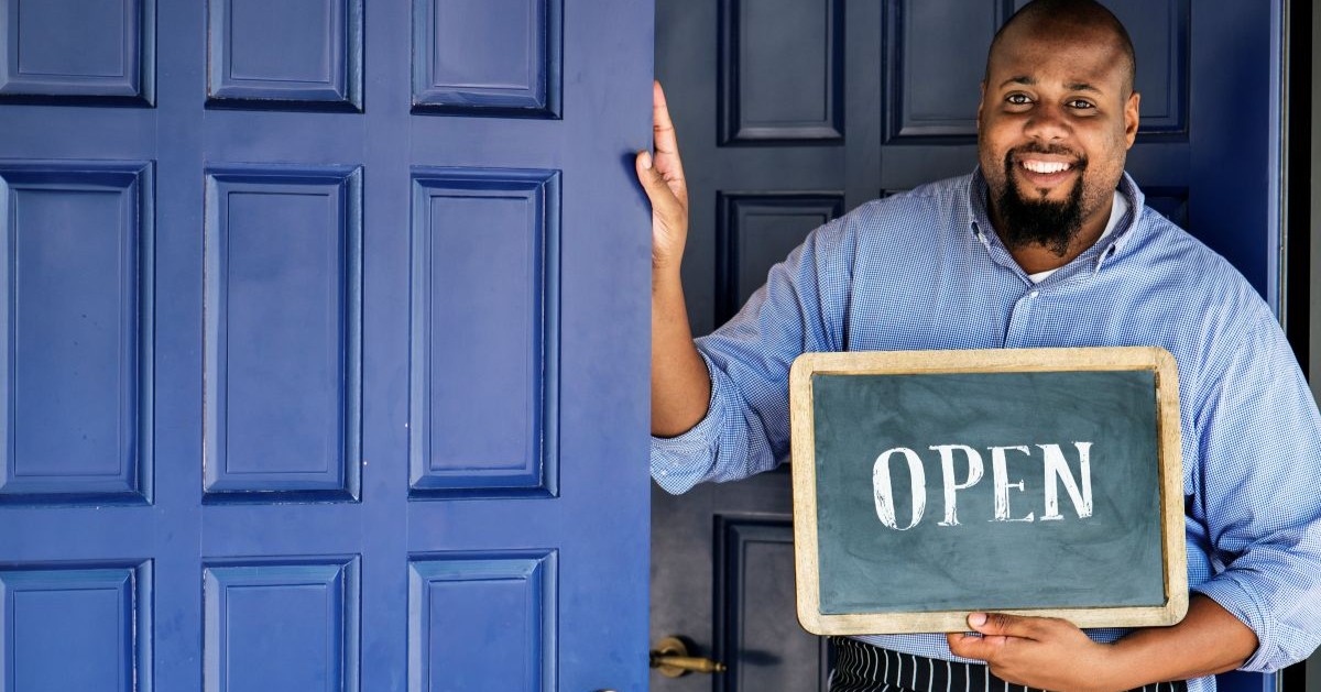 small-business-owner-open-sign-1200×628 Cafe owner with an Open sign.